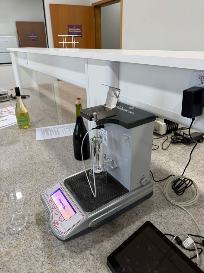 Bancada do laboratório com equipamento de análise, garrafas de vinho e balança de precisão